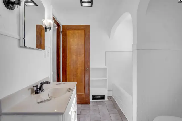 Bright bathroom with white vanity, dark tile floor, and arched doorway.