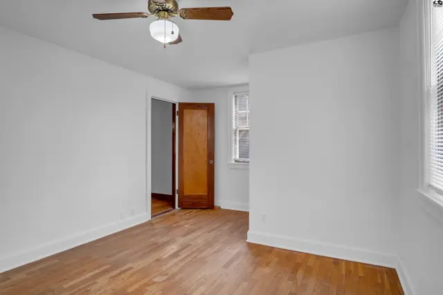 Bright bedroom with hardwood floors, white walls, and a wooden door leading to another room.