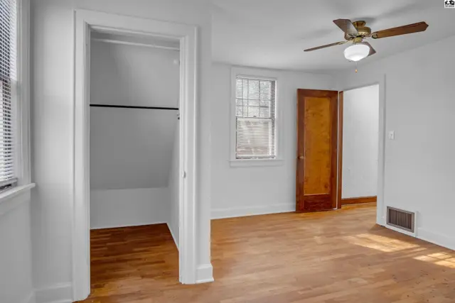 Bright bedroom with hardwood floors, ceiling fan, and a view into a spacious closet.
