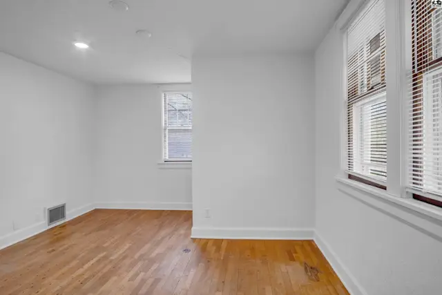 Bright room with hardwood floors, white walls, and two windows with blinds.