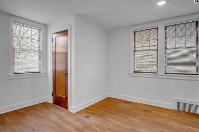 Bright room with hardwood floors, white walls, and three windows with blinds.