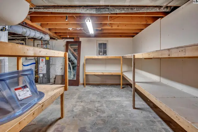 Basement storage area with concrete floor, exposed wooden beams, and built-in shelving.