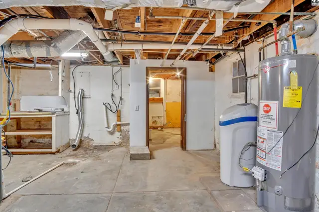 Unfinished basement with concrete floors, exposed pipes, water heater, and utility sink.