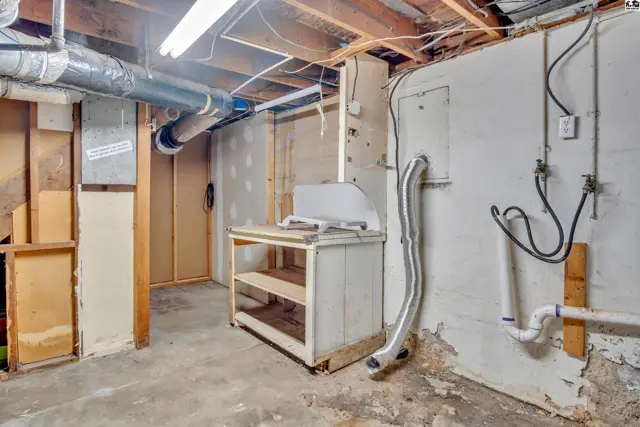 Unfinished basement with exposed pipes, concrete floor, and utility sink.
