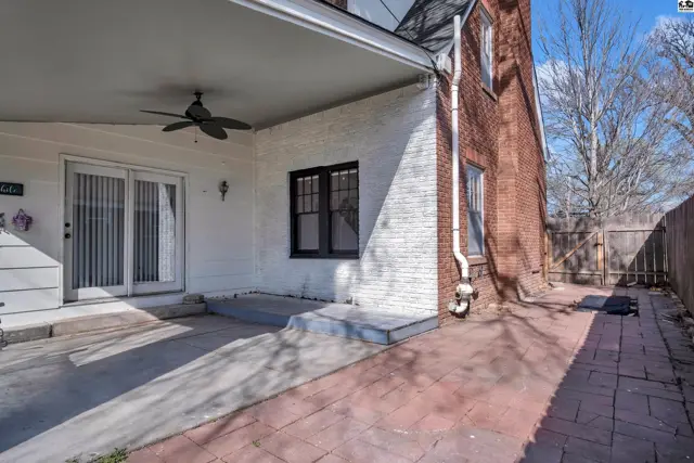 Covered patio with ceiling fan and brick walkway adjacent to a red brick house.
