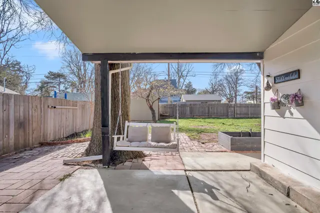 Covered patio with a swing, brick and concrete flooring, and a fenced backyard.