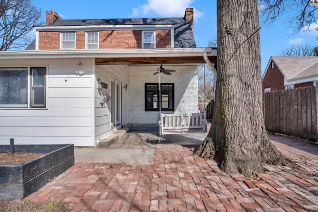 White-sided home exterior with brick patio, covered porch, and large tree.
