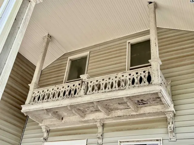 Ornate white balcony with decorative railing and columns adorns the exterior of a home.
