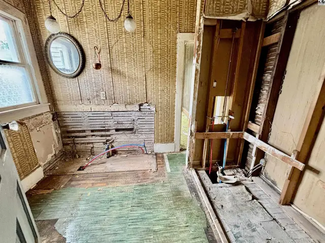 Renovation in progress shows exposed studs, plumbing, and vintage wallpaper in a room with a round mirror.