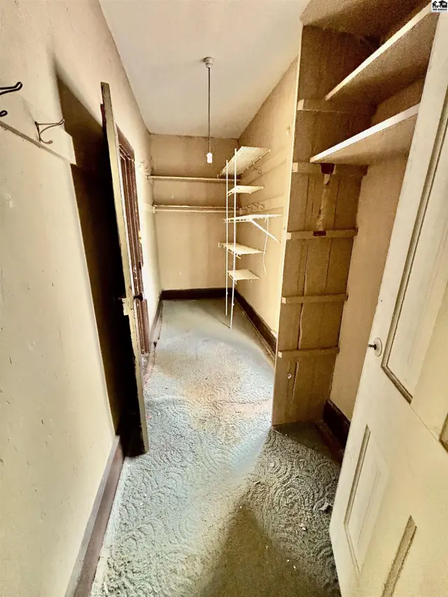 Hallway with built-in shelving, patterned carpet, and cream-colored walls.
