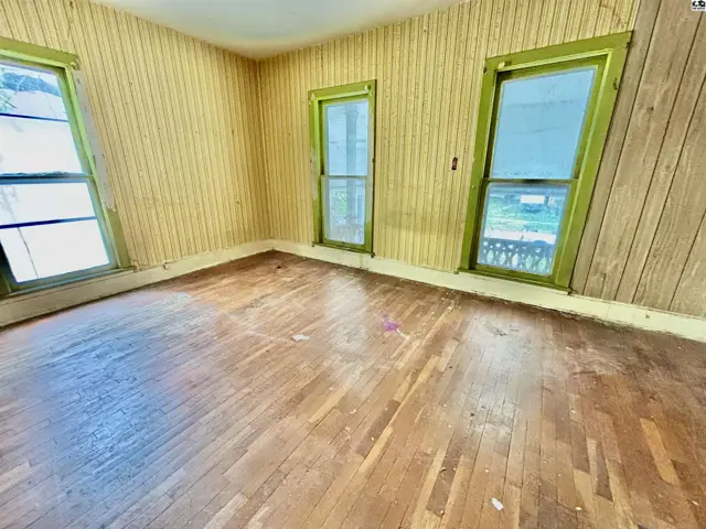 Empty room with wood floors, yellow striped wallpaper, and green-trimmed windows.