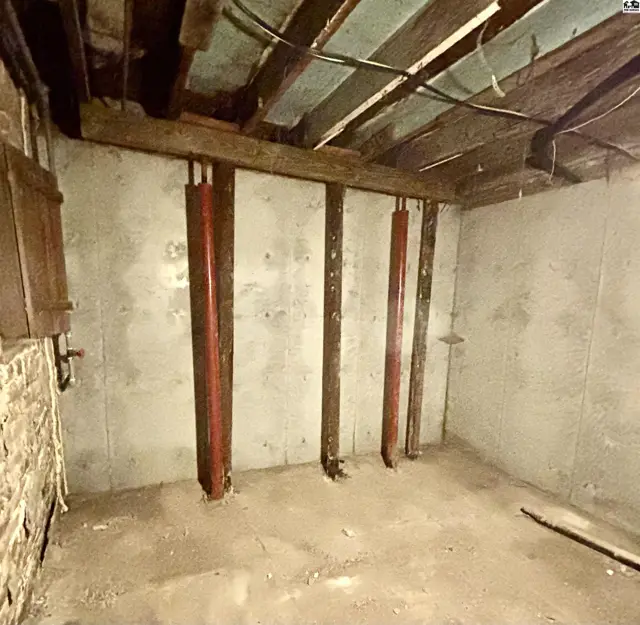 Concrete basement walls with red steel support beams and exposed wooden ceiling joists.