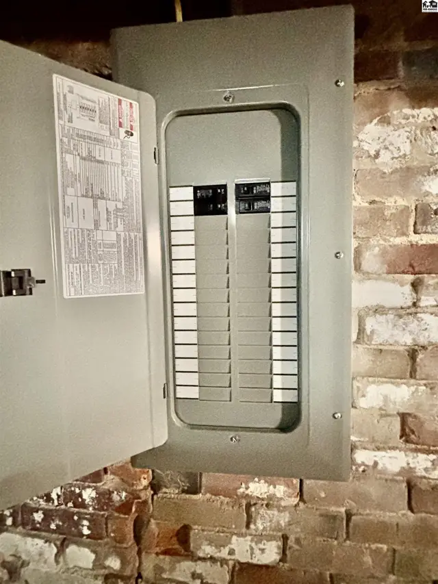 Open electrical panel with breakers on a brick wall.