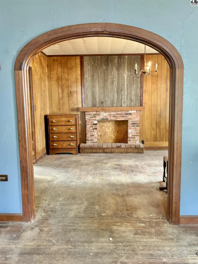 Archway reveals a living room with wood paneling, brick fireplace, and hardwood floors.