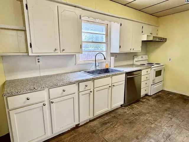 Kitchen with white cabinets, granite countertops, stainless steel dishwasher, and white appliances.