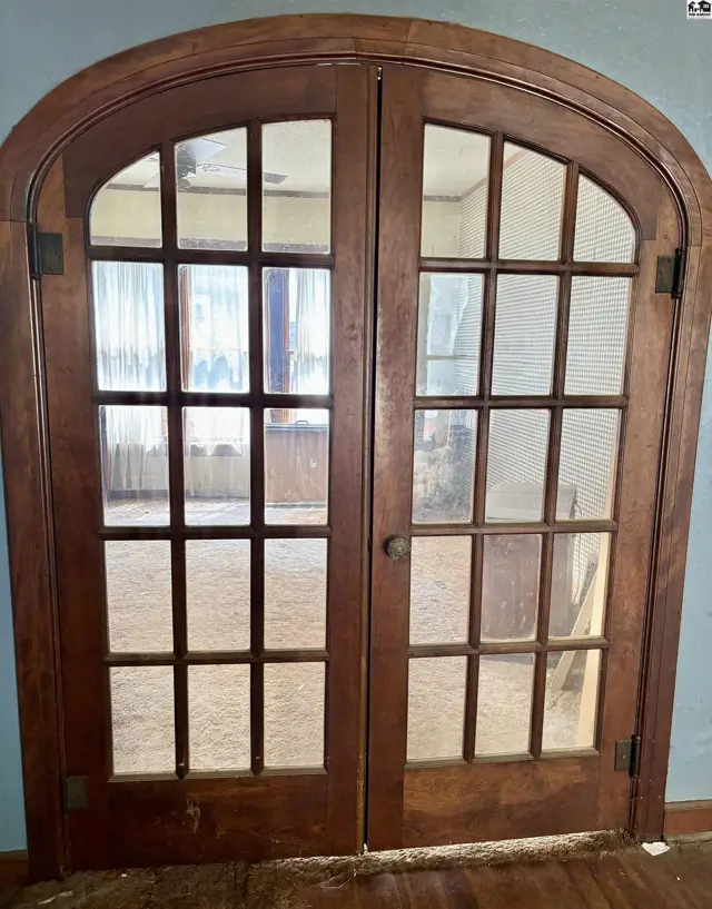 Arched wooden double doors with glass panes open to a room with carpet and curtains.