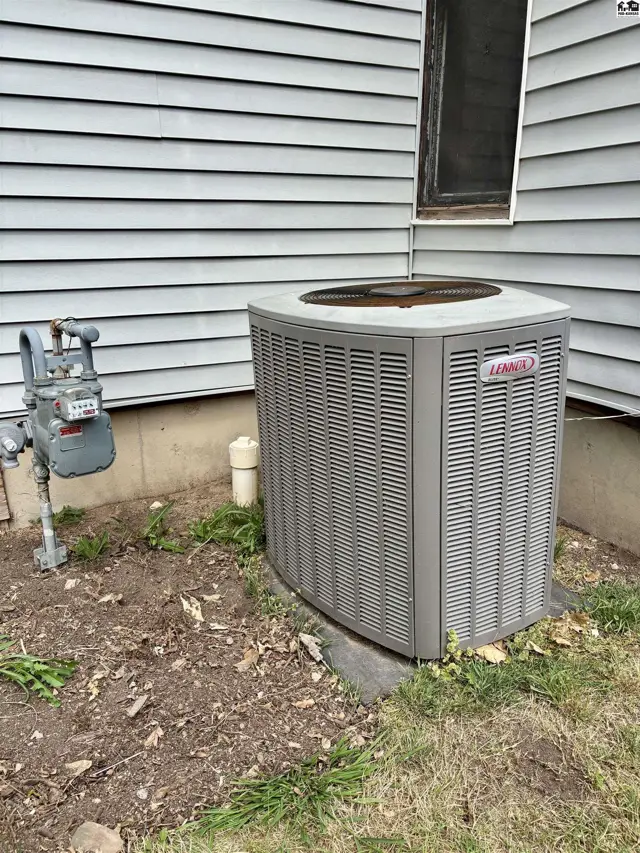 Exterior view of a gray Lennox air conditioning unit next to a gas meter and siding.
