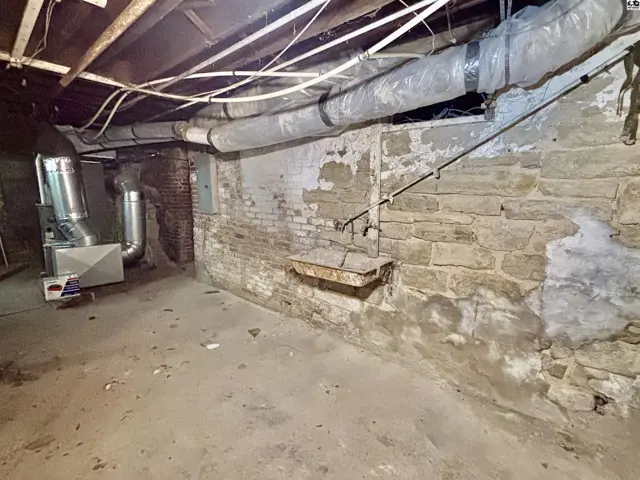 Basement with exposed stone walls, unfinished concrete floor, and HVAC system.