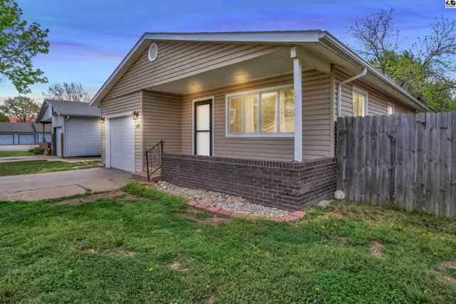 Exterior view of a tan vinyl-sided house with a brick foundation and a covered front porch.