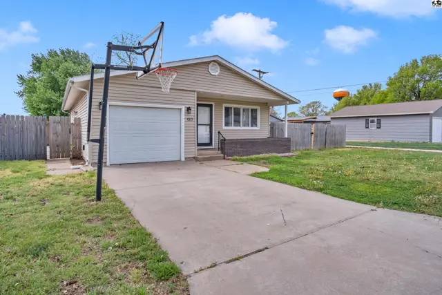 Tan vinyl-sided ranch home with a garage, basketball hoop, and concrete driveway.