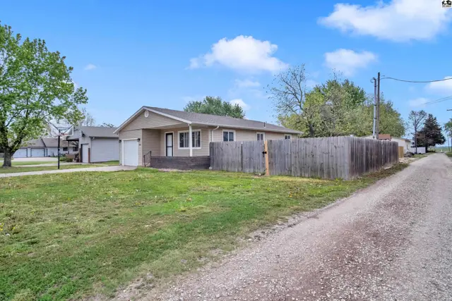 Tan stucco ranch home with a covered porch, attached garage, and wooden privacy fence.