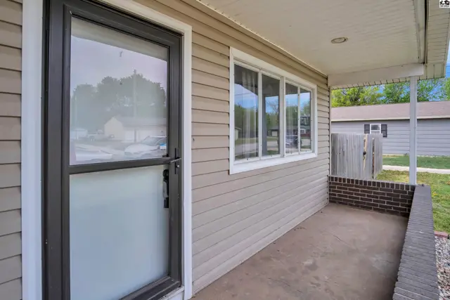 Exterior view of a home with tan siding, a covered porch, and a glass-paneled front door.