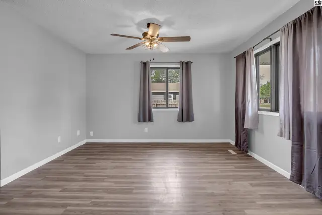 Spacious room with light gray walls, wood-look laminate flooring, and a ceiling fan.