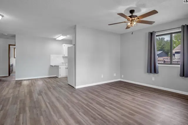 Spacious living area with gray walls, wood-look flooring, and a ceiling fan.