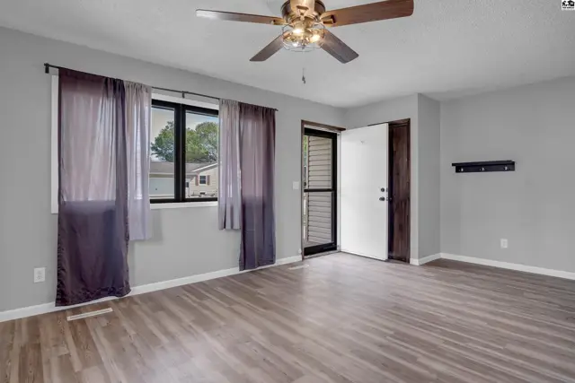 Living room with gray walls, wood-look flooring, a ceiling fan, and a view through the front door.
