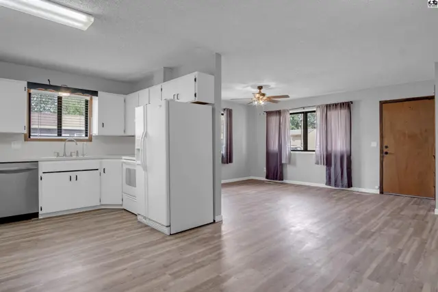 Bright kitchen with white cabinets and appliances opens to a spacious living area with wood-look flooring.