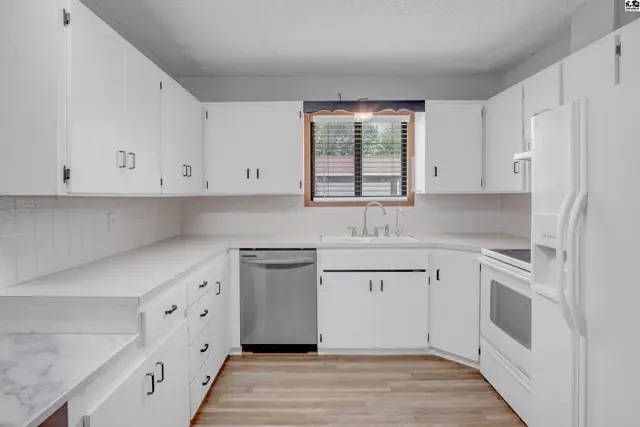 Bright white kitchen with ample cabinetry, stainless steel appliances, and light wood flooring.