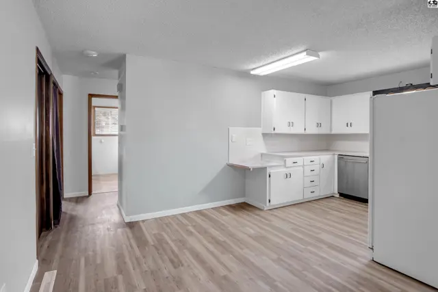 Bright kitchen with white cabinets, light wood laminate flooring, and a stainless steel dishwasher.