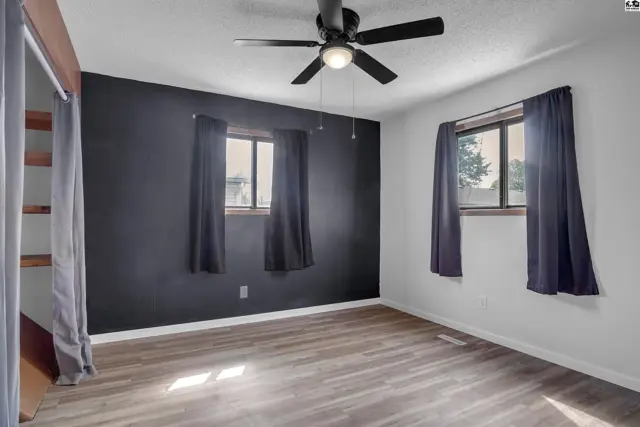 Spacious bedroom with dark accent wall, wood-look flooring, and two windows with dark curtains.