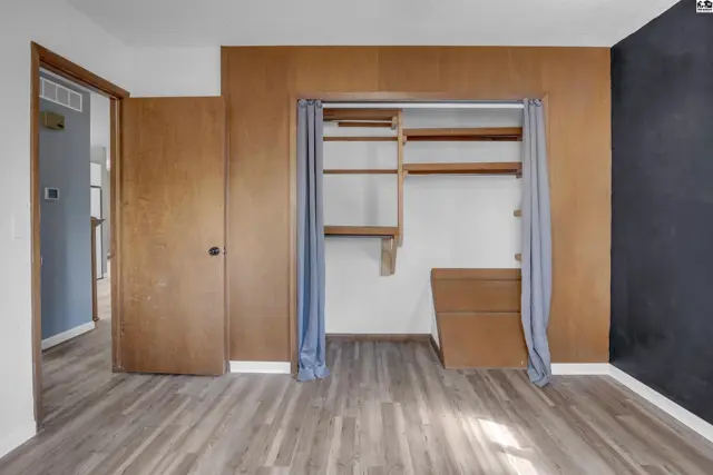 Bedroom with wood-paneled walls, open closet with shelves, and wood-look flooring.