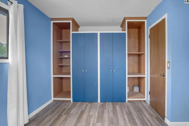 Built-in blue cabinets and open shelving flank a closet in a room with blue walls and wood-look flooring.