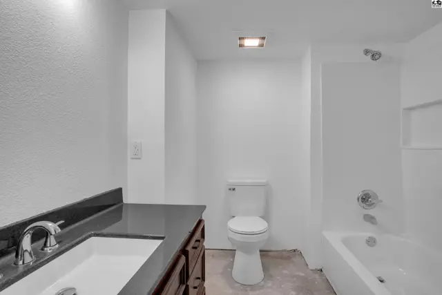 Modern bathroom with white walls, dark granite vanity, and a white toilet and bathtub.
