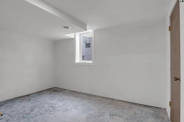 Unfinished basement room with concrete floor, white walls, and a small window.