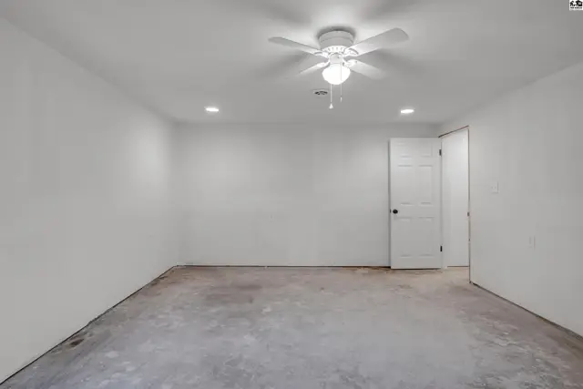 Empty room with white walls, concrete floor, ceiling fan, and recessed lighting.