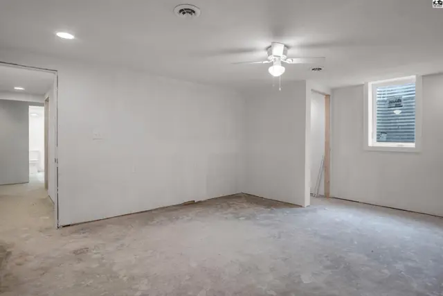 Unfinished basement room with white walls, concrete floor, and a ceiling fan.