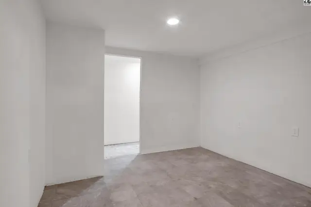 Bright, unfinished room with white walls and concrete floors, leading to another bright space.