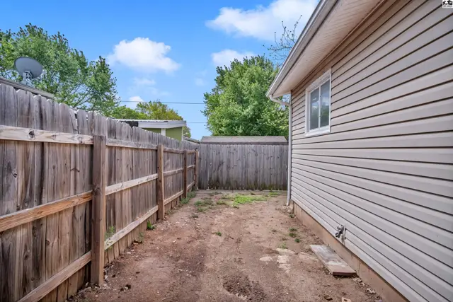 Wooden fence encloses a backyard with beige vinyl siding and a window.