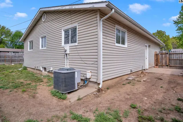 Exterior view of a beige vinyl-sided house with white trim, a detached AC unit, and a wooden fence.