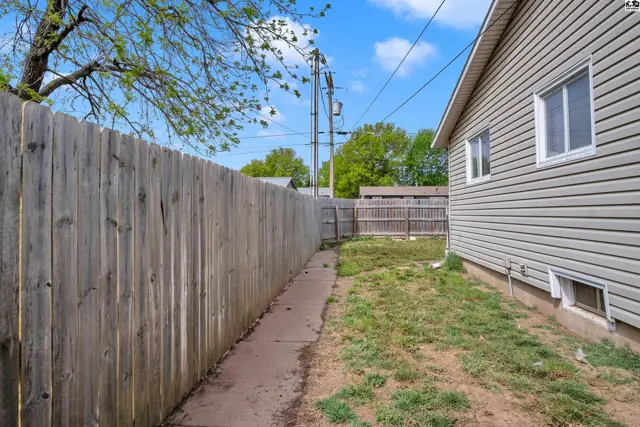 Exterior view of a home with vinyl siding, a wooden fence, and a narrow concrete path.