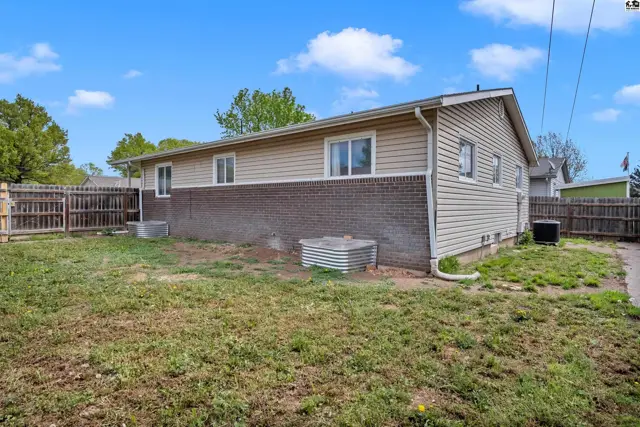 Exterior view of a house with tan siding, brick lower level, and a fenced backyard.
