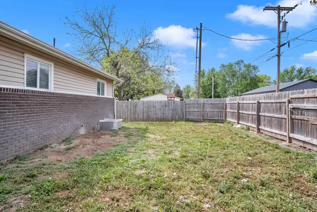 Fenced backyard with a brick retaining wall and a wooden fence under a bright blue sky.