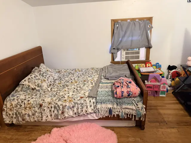 Wooden bed with floral bedding sits in a room with hardwood floors.