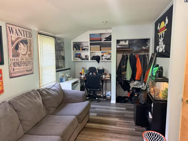This room features a sofa, desk, shelving, and a closet with hanging clothes.