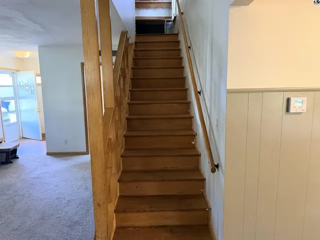 Wooden stairs with a natural wood railing ascend to an upper level.