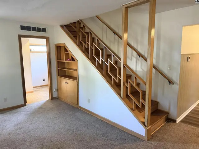 Carpeted floor leads to a wooden staircase with decorative railing and built-in shelving.