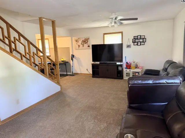 Spacious living area with carpet, a wooden staircase, and a ceiling fan.